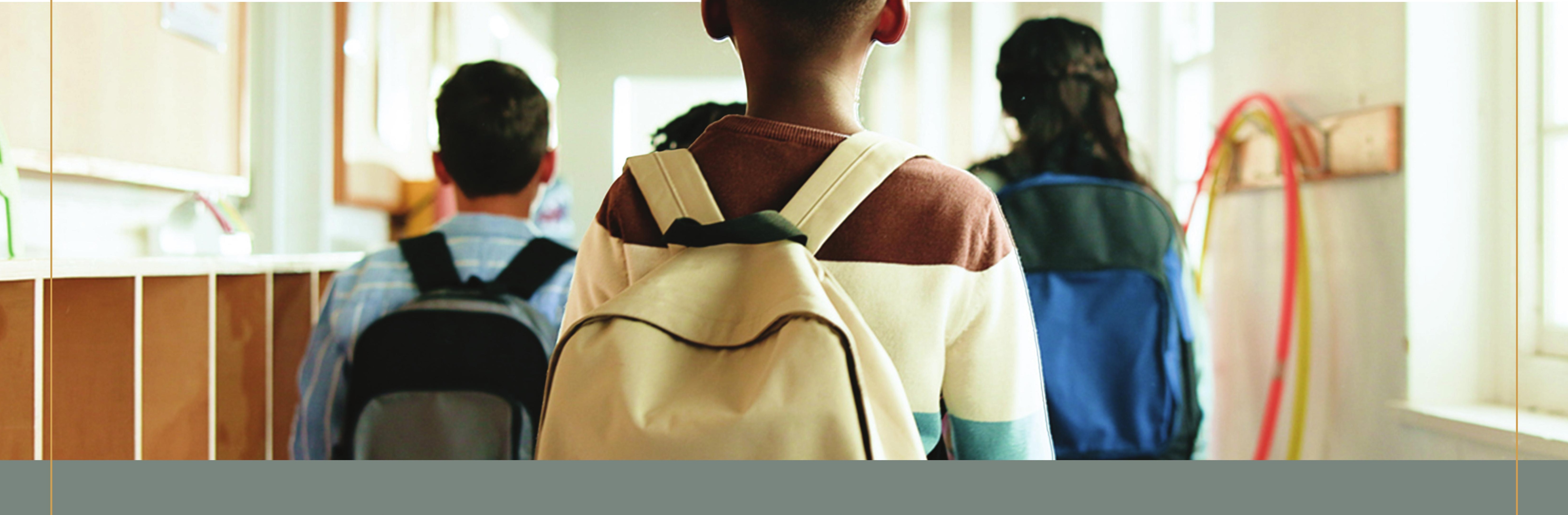 Students walking down a school hallway wearing backpacks